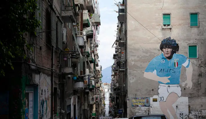 The historic mural artwork of the 1990 Serie A Scudetto won by Napoli dominates the small and picturesque square of Largo degli Artisti in the Quartieri Spagnoli, from which Vesuvius is partially visible. Naples, Italy. August 2020.