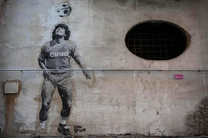 The image of Maradona juggling with the ball during a warm-up training during his first season at Napoli, re-elaborated by street artist San Spiga, stands out on a peeling wall in the Quartieri Spagnoli. Naples, Italy. August 2020.