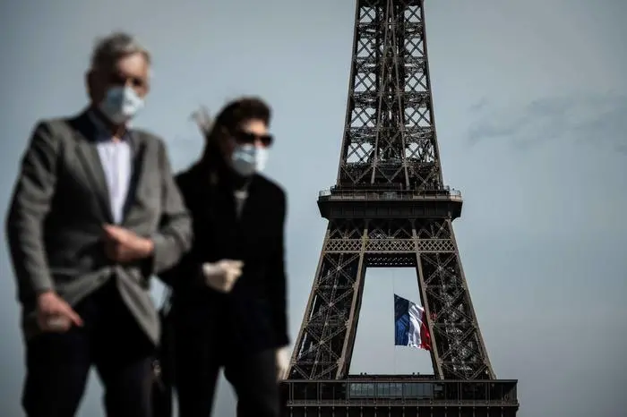 (FILES) In this file photo taken on May 11, 2020, a man and a woman wearing face masks walk on Trocadero Plaza as a French national flag flies on the Eiffel Tower in background in Paris on the first day of France's easing of lockdown measures in place for 55 days to curb the spread of the COVID-19 pandemic, caused by the novel coronavirus. - Wearing a mask will be compulsory in parts of Paris and its wider region from August 10, 2020, to combat a rise in coronavirus infections in and around the French capital, the police said. The mask will be obligatory for all those aged 11 and over from 8:00 am (0600 GMT) on August 10 \\\"in certain very crowded zones\\\", the police said in a statement on August 8, without yet detailing which areas were affected. (Photo by PHILIPPE LOPEZ / AFP)
