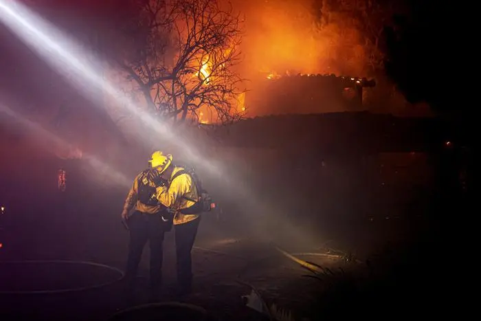 Firefighters recoil from smoke and heat from a fully engulfed house on Jolette Way in Granada Hills North early Friday morning, Oct. 11, 2019. (David Crane/The Orange County Register via AP) [CopyrightNotice: Los Angeles Daily News/SCNG]