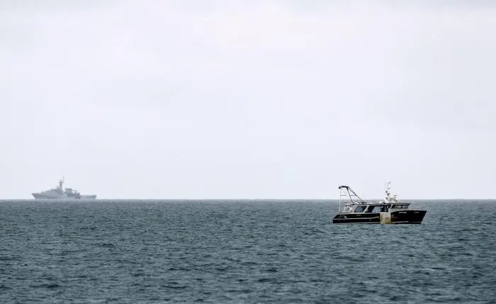 HMS Tamar (REAR), a Batch 2 river-class offshore patrol vessel of the British Navy, is watched by a fishing boat as it patrols the waters off the British island of Jersey on May 6, 2021. - Around 50 French fishing boats gathered to protest at the main port of the UK island of Jersey on May 6, amid fresh tensions between France and Britain over fishing. The boats massed in front of the port of Saint Helier to draw attention to what they see as unfair restrictions on their ability to fish in UK waters after Brexit, an AFP photographer at the scene said. (Photo by Sameer Al-DOUMY / AFP)