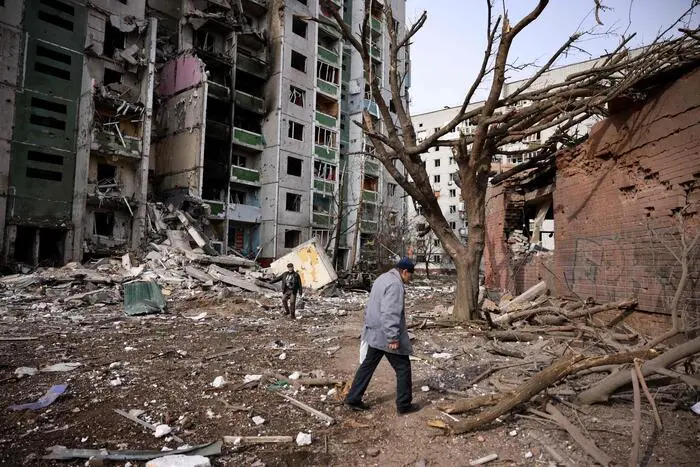Men walk past a residential building damaged in yesterday's shelling in the city of Chernihiv on March 4, 2022. - Fourty-seven people died on March 3 when Russian forces hit residential areas, including schools and a high-rise apartment building, in the northern Ukrainian city of Chernihiv, officials said. (Photo by Dimitar DILKOFF / AFP)