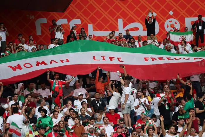 Iran supporters wave their national flag bearing the word \\\"Woman, Life, Freedom\\\" as they cheer during the Qatar 2022 World Cup Group B football match between England and Iran at the Khalifa International Stadium in Doha on November 21, 2022. (Photo by FADEL SENNA / AFP)