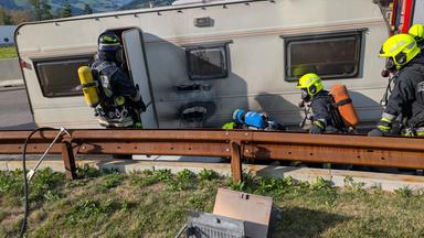 Roulotte in fiamme sull'autostrada del Brennero con vigili del fuoco al lavoro, fumo denso e traffico bloccato