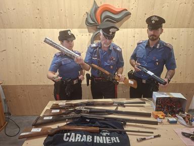 Interno di un'abitazione con armi sequestrate, fucili e munizioni su tavolo, operazione polizia