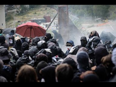 Polizia in tenuta antisommossa durante scontri in strada in montagna, manifestanti, danni e disordini urbani, immagine di approfondimento